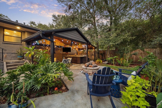 patio terrace at dusk with an outdoor fire pit, area for grilling, and a fenced backyard