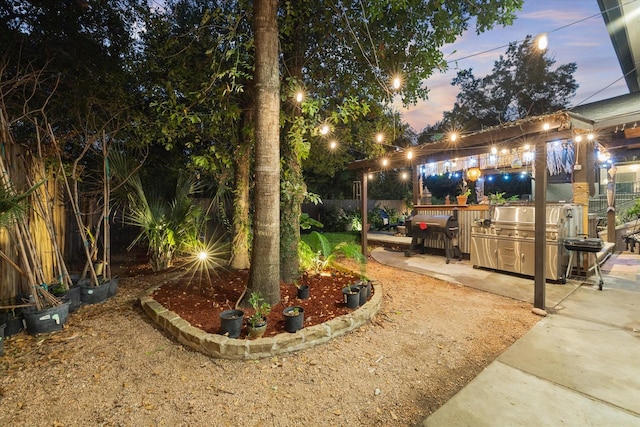 yard at dusk featuring a patio area, fence, and exterior kitchen