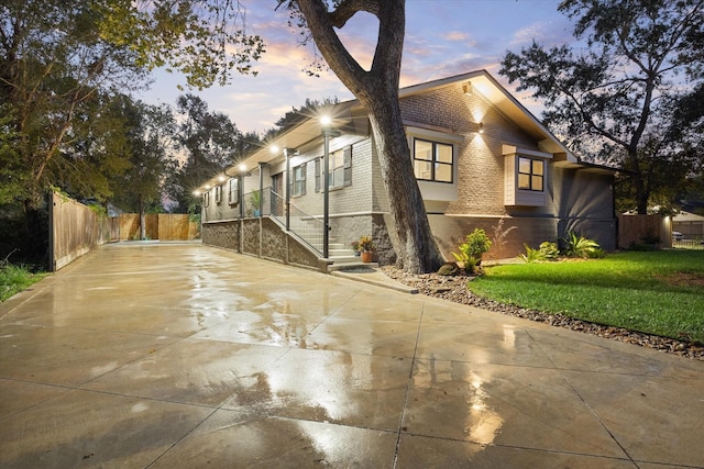 view of side of home featuring brick siding, fence, concrete driveway, stairway, and a lawn