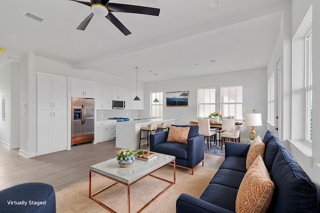 living room featuring beamed ceiling, ceiling fan, and light hardwood / wood-style flooring