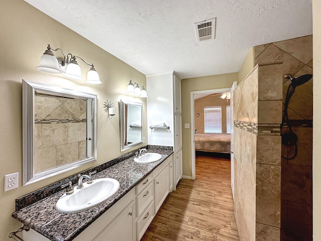 bathroom with vanity, hardwood / wood-style flooring, a tile shower, and a textured ceiling