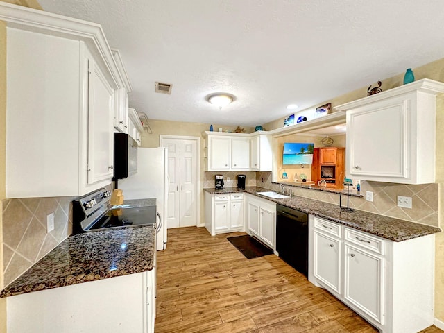 kitchen with light hardwood / wood-style floors, white cabinets, black dishwasher, dark stone counters, and sink