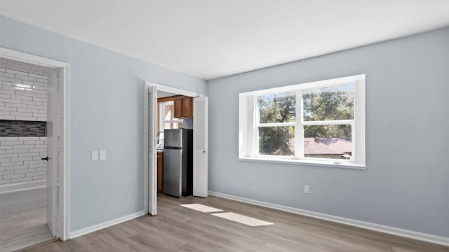 unfurnished bedroom featuring ensuite bath, stainless steel fridge, and light wood-type flooring