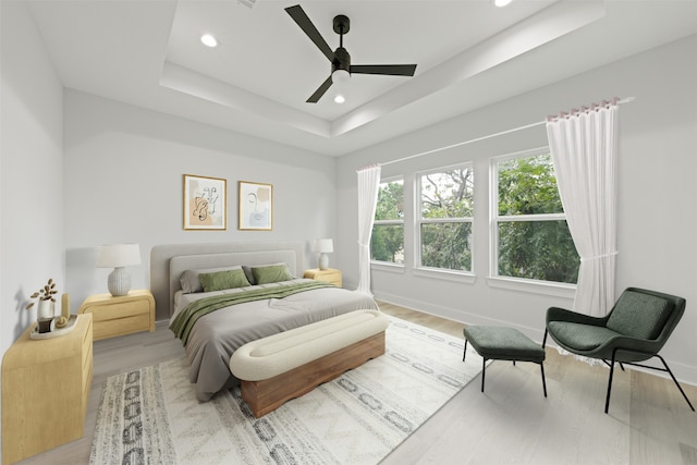 bedroom featuring light wood-type flooring, a raised ceiling, and ceiling fan