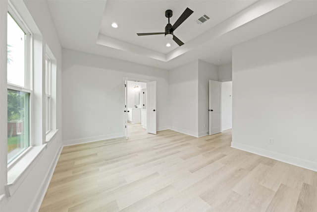 spare room with light wood-type flooring, ceiling fan, and a raised ceiling