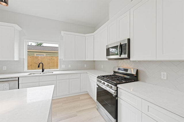 kitchen with appliances with stainless steel finishes, light hardwood / wood-style floors, tasteful backsplash, white cabinets, and sink