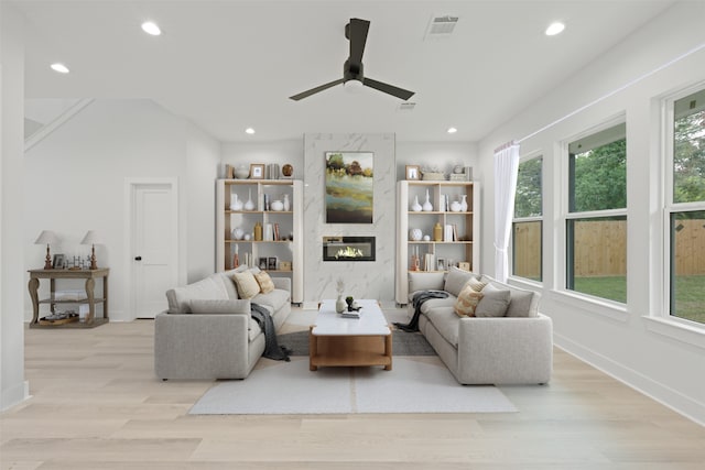 living room featuring light wood-type flooring, ceiling fan, and a premium fireplace