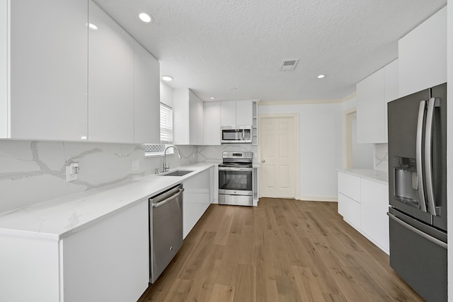 kitchen featuring white cabinetry, sink, stainless steel appliances, decorative backsplash, and light wood-type flooring