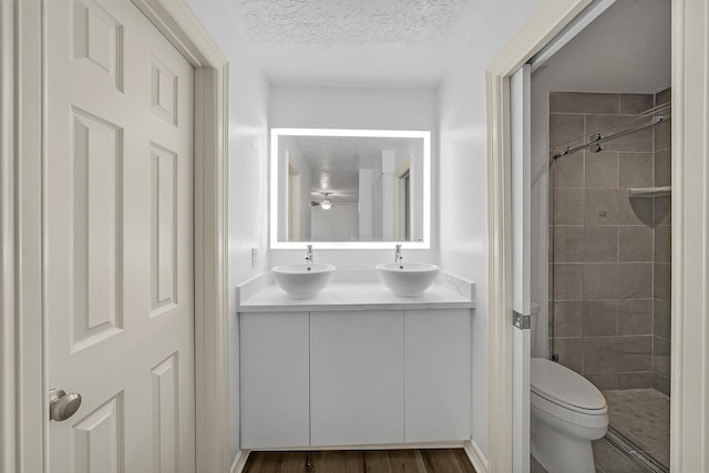 bathroom with vanity, hardwood / wood-style flooring, toilet, tiled shower, and a textured ceiling