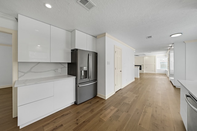 kitchen with crown molding, a textured ceiling, appliances with stainless steel finishes, light hardwood / wood-style floors, and white cabinetry