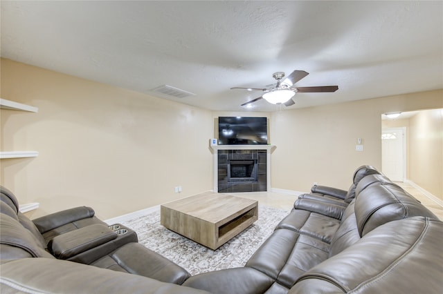 living room with ceiling fan, a textured ceiling, and a tile fireplace