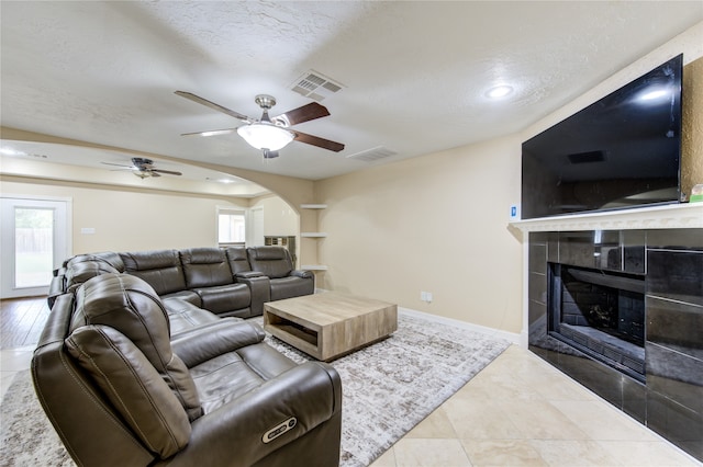 tiled living room with a textured ceiling, lofted ceiling, a tiled fireplace, and ceiling fan