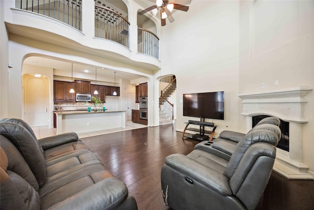 living room featuring ceiling fan, light wood-type flooring, a high end fireplace, and a high ceiling