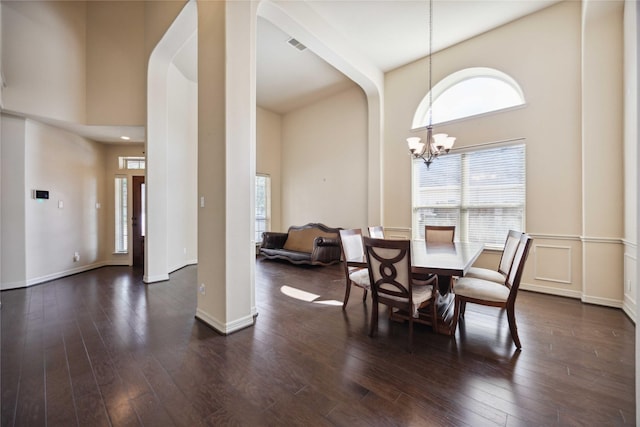 dining area with dark wood-type flooring, a high ceiling, and an inviting chandelier