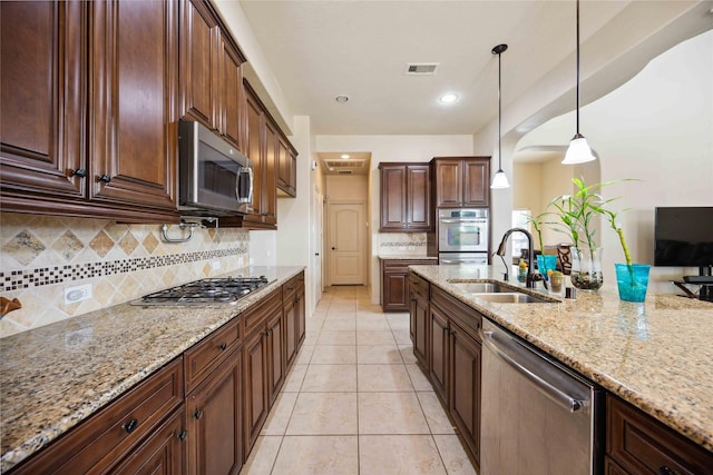 kitchen with appliances with stainless steel finishes, light tile patterned flooring, light stone countertops, pendant lighting, and sink