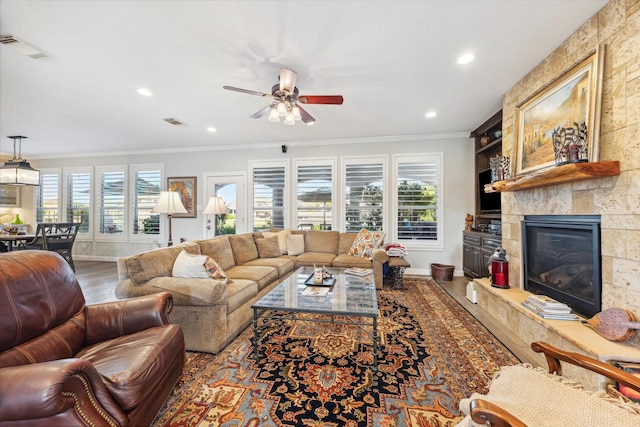 living room featuring a large fireplace, ornamental molding, hardwood / wood-style flooring, and ceiling fan