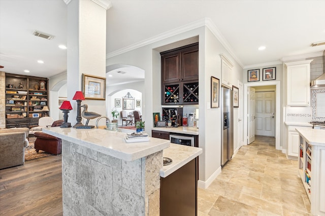 kitchen featuring light stone counters, stainless steel refrigerator with ice dispenser, dark brown cabinets, and crown molding