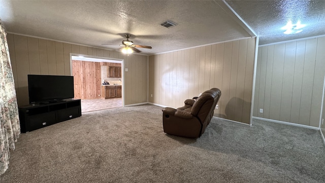 sitting room featuring ceiling fan, a textured ceiling, wooden walls, and carpet flooring