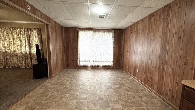 empty room featuring a drop ceiling and wood walls