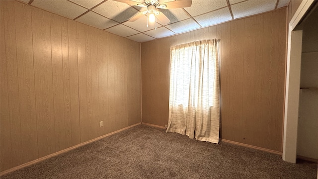 spare room with ceiling fan, wooden walls, and a drop ceiling