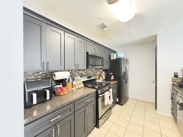 kitchen featuring decorative backsplash, gray cabinetry, light tile patterned floors, stainless steel appliances, and a textured ceiling