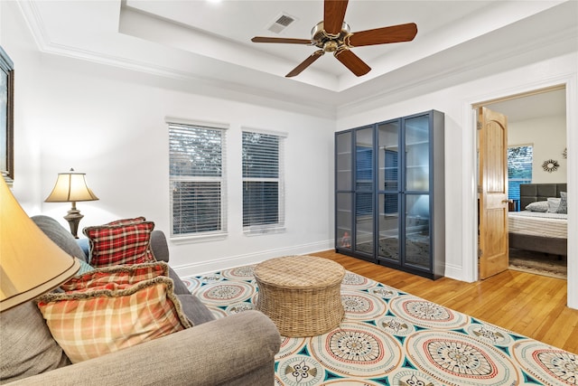 living area featuring hardwood / wood-style floors, a raised ceiling, ceiling fan, and a healthy amount of sunlight