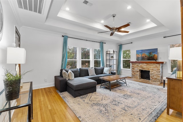 living room featuring hardwood / wood-style floors, a raised ceiling, a stone fireplace, ceiling fan, and ornamental molding