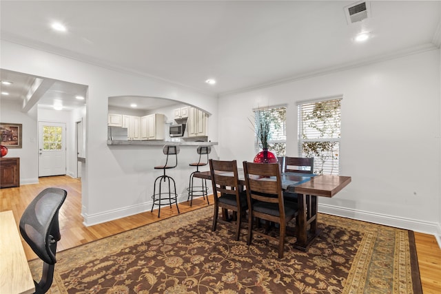 dining space with beamed ceiling, light hardwood / wood-style floors, and ornamental molding