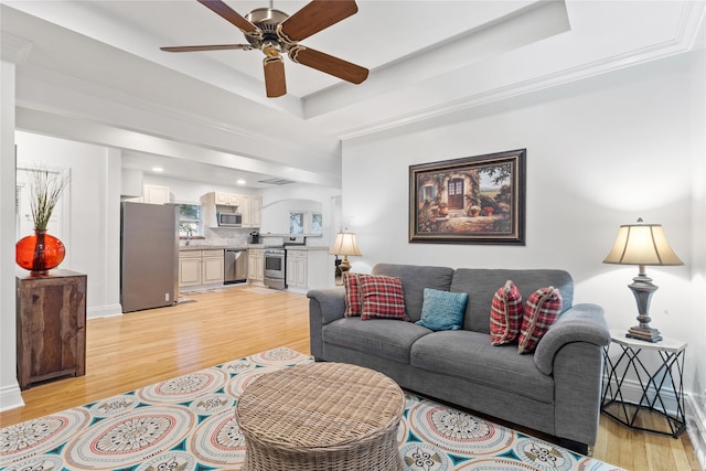 living room featuring light hardwood / wood-style floors, ceiling fan, and a tray ceiling