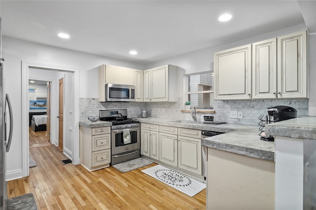 kitchen with tasteful backsplash, sink, stainless steel appliances, and light hardwood / wood-style floors