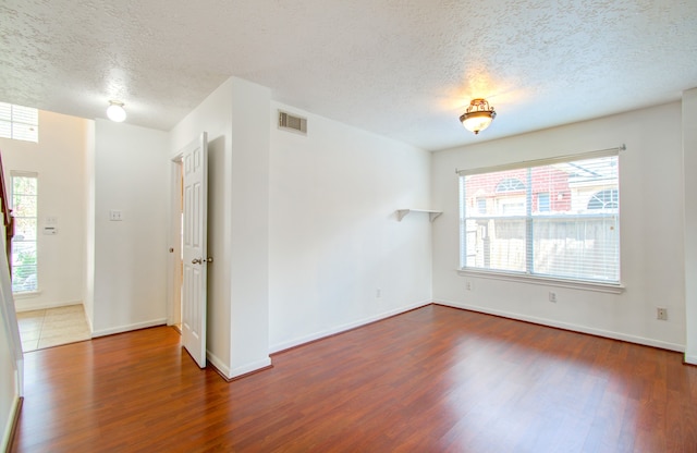 spare room with a textured ceiling, dark hardwood / wood-style floors, and a wealth of natural light