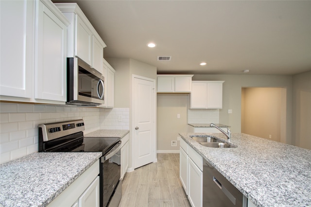 kitchen with appliances with stainless steel finishes, white cabinetry, light stone counters, light wood-type flooring, and sink