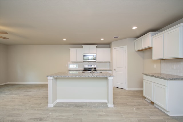 kitchen with ceiling fan, white cabinets, a center island with sink, and stainless steel appliances