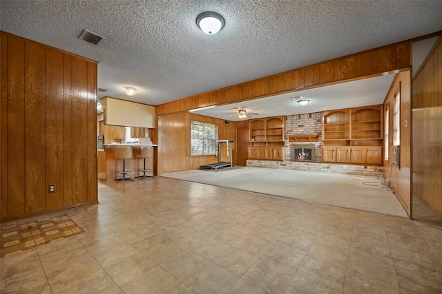 unfurnished living room featuring a brick fireplace, wooden walls, built in shelves, and ceiling fan