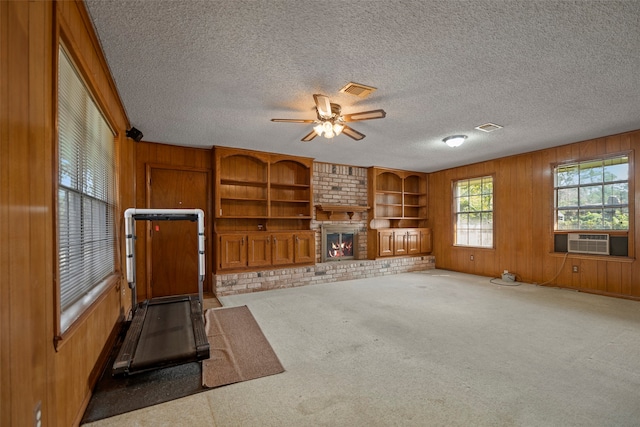 unfurnished living room with ceiling fan, a textured ceiling, a fireplace, and wood walls