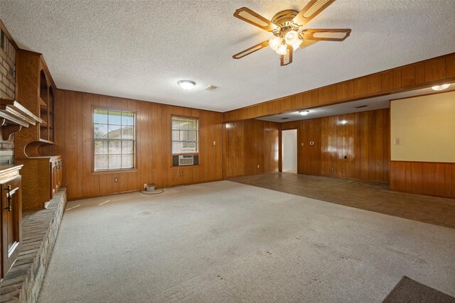 carpeted spare room with a fireplace, a textured ceiling, cooling unit, ceiling fan, and wooden walls