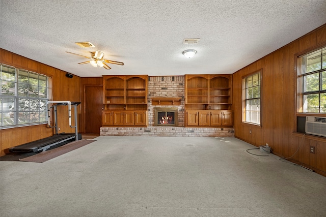 interior space with wood walls, ceiling fan, light colored carpet, and a brick fireplace