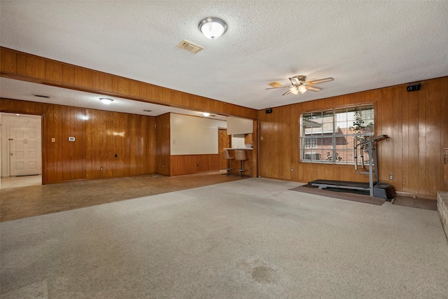 workout area featuring ceiling fan, a textured ceiling, wooden walls, and carpet