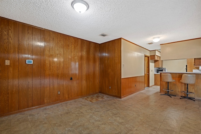 empty room featuring wooden walls, a textured ceiling, and bar