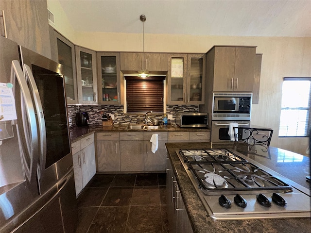 kitchen with appliances with stainless steel finishes, tasteful backsplash, pendant lighting, dark stone counters, and sink