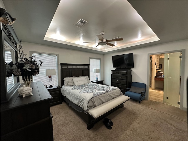 bedroom with a raised ceiling, light carpet, and ceiling fan