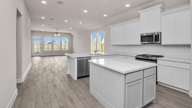 kitchen with a center island, kitchen peninsula, stainless steel appliances, and white cabinetry