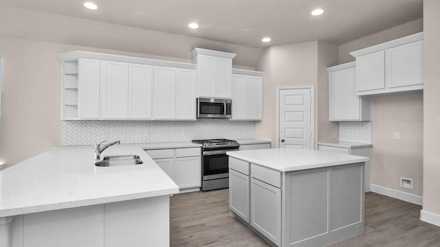 kitchen featuring kitchen peninsula, appliances with stainless steel finishes, sink, white cabinets, and a kitchen island