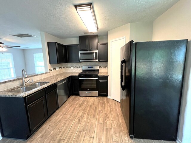 kitchen with light hardwood / wood-style floors, stainless steel appliances, a textured ceiling, ceiling fan, and sink