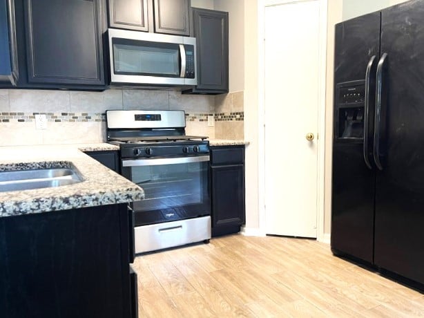 kitchen featuring light stone counters, backsplash, light wood-style floors, and appliances with stainless steel finishes