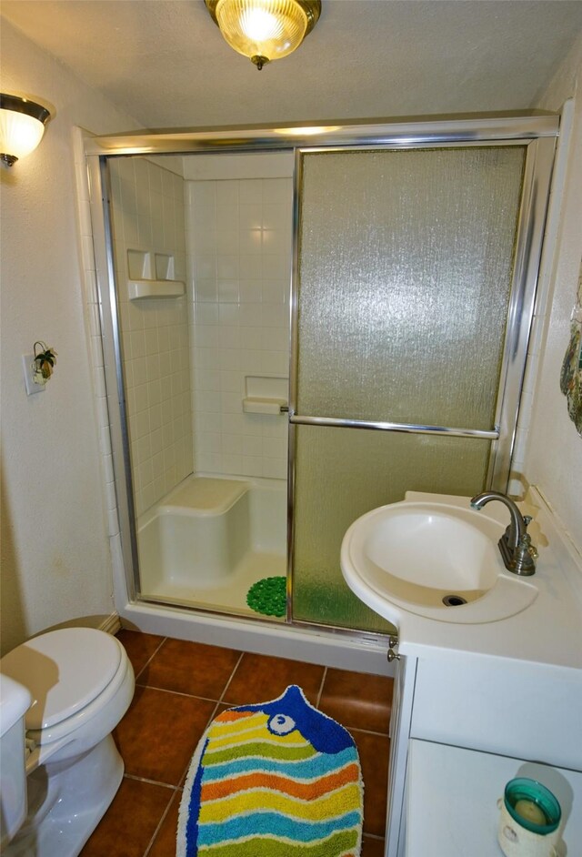 bathroom featuring tile patterned flooring, a shower with shower door, vanity, and toilet