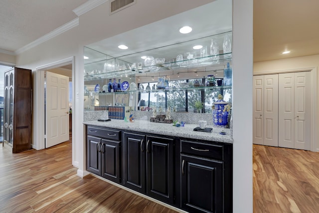 bar featuring backsplash, light stone countertops, light hardwood / wood-style floors, and crown molding