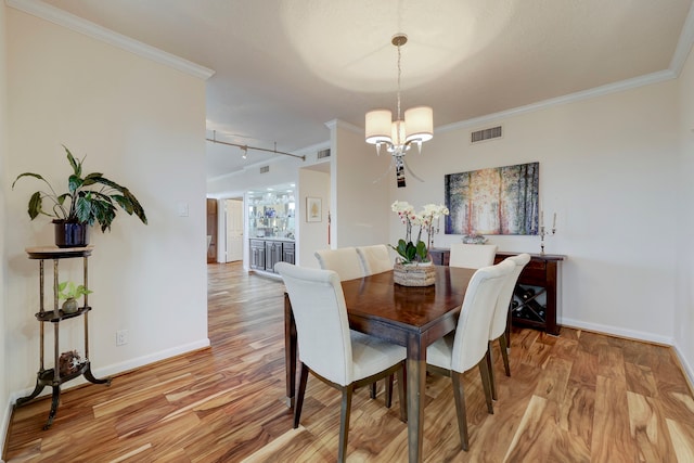 dining room featuring track lighting, light hardwood / wood-style floors, crown molding, and an inviting chandelier