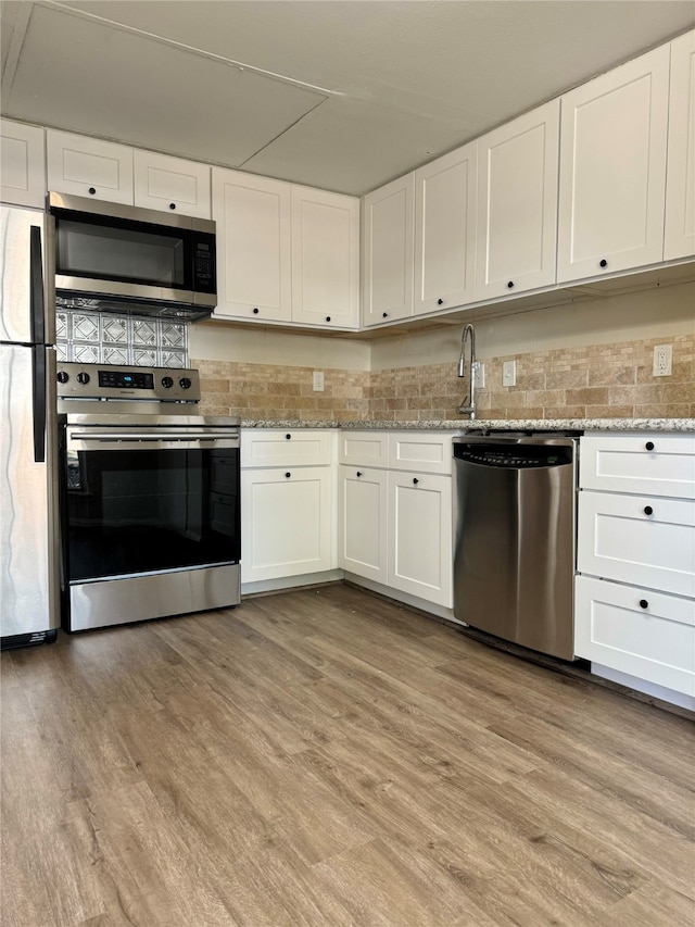 kitchen featuring light wood-type flooring, white cabinets, backsplash, appliances with stainless steel finishes, and light stone countertops