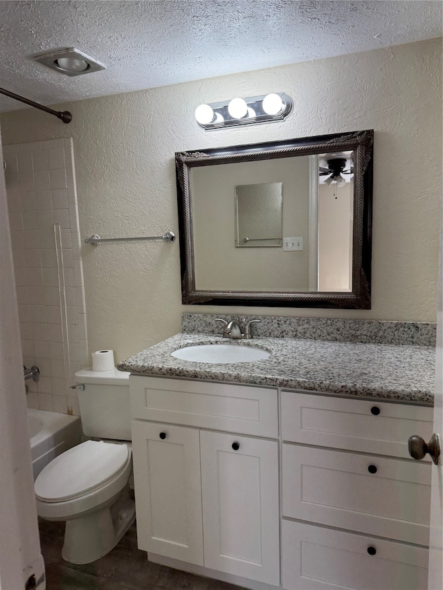 full bathroom with a textured ceiling, bathing tub / shower combination, ceiling fan, vanity, and toilet